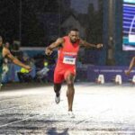 Cameroons Emmanuel Eseme in red sprints to gold in the Mens 100m final at Scotstoun Stadium during the 2026 Commonwealth Games in Glasgow Scotland on July 28 2026 ahead of South Africas Akani Simbine in green and Nigerias Kayinsola Ajayi in green and white on a wet rain soaked track  trybalnews