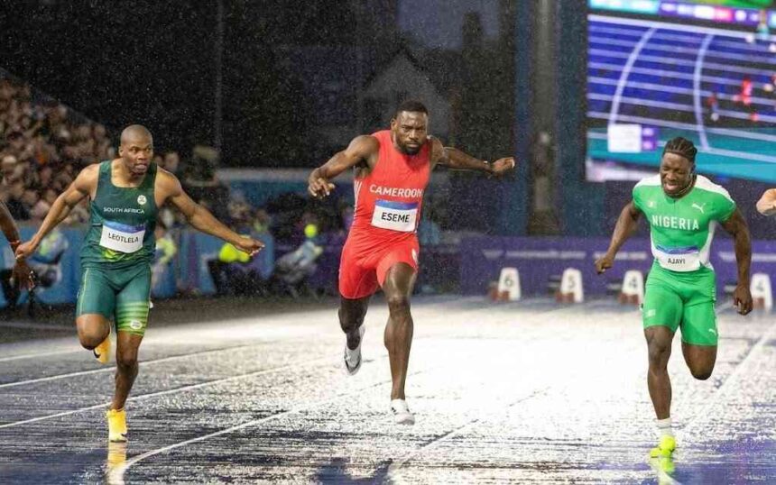 Cameroons Emmanuel Eseme in red sprints to gold in the Mens 100m final at Scotstoun Stadium during the 2026 Commonwealth Games in Glasgow Scotland on July 28 2026 ahead of South Africas Akani Simbine in green and Nigerias Kayinsola Ajayi in green and white on a wet rain soaked track  trybalnews