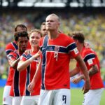 Norway striker Erling Haaland wearing jersey number 9 celebrates with teammates after scoring his teams first goal The players are grouped together on the pitch at New York New Jersey Stadium during the FIFA World Cup 2026 Round of 16 match between Brazil and Norway on July 5 2026 Stadium crowd and green turf are visible in the background  trybalnews