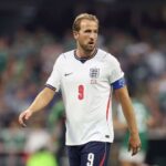 England captain Harry Kane wearing jersey number 9 and a white England kit with navy shorts walks on the pitch during play He wears a blue captains armband and looks ahead with a focused expression during the FIFA World Cup 2026 Round of 16 match between Mexico and England at Mexico City Stadium on July 5 2026 Blurred crowd and players in green are visible in the background  trybalnews