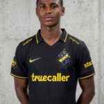 Portrait of a young man in a black AIK football jersey with yellow trim standing against a concrete wall The kit features the AIK crest and the sponsor truecaller in yellow  trybalnews