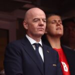 Bald man in a dark suit and tie with a FIFA pin looking ahead at a formal event  trybalnews