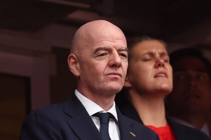 Bald man in a dark suit and tie with a FIFA pin, looking ahead at a formal event.