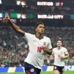 England midfielder Jude Bellingham wearing a white jersey number 10 and navy shorts points to the sky with his right arm as he celebrates He has just scored Englands first goal during the FIFA World Cup 2026 Round of 16 match between Mexico and England at Mexico City Stadium on July 5 2026 England teammate Declan Rice wearing number 4 runs behind him with a packed stadium and MEXICO CITY on the scoreboard in the background  trybalnews