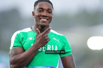 Smiling male athlete in a green Nigeria jersey giving a thumbs-up in the rain outdoors.