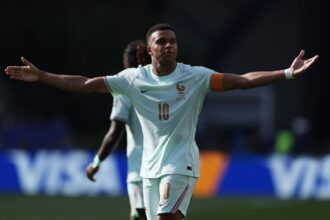 France forward Kylian Mbappe, wearing a light blue #10 jersey and orange captain's armband, celebrates with arms outstretched after scoring France's first goal in the FIFA World Cup 2026 Quarter Final match against Morocco at Boston Stadium in Foxborough, Massachusetts on July 9, 2026.