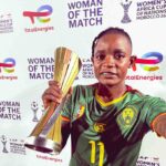 Young woman soccer player in a green Cameroon jersey holds a tall gold trophy at a Women of the Match event  trybalnews