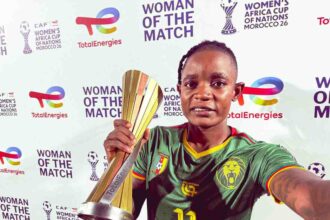 Young woman soccer player in a green Cameroon jersey holds a tall gold trophy at a Women of the Match event.
