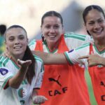 Three female soccer players celebrate together on the field arms around each other and smiling wearing white and green jerseys with orange bibs  trybalnews