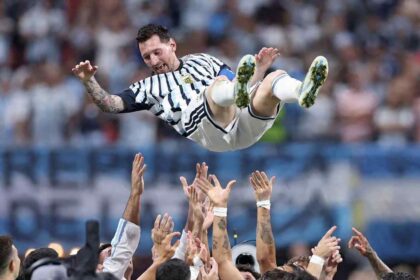 Lionel Messi, wearing Argentina's blue and white striped #10 jersey, is lifted into the air by teammates after Argentina's 3-2 victory over Egypt in the FIFA World Cup 2026 Round of 16 at Atlanta Stadium in Atlanta, Georgia on July 7, 2026. Messi smiles with arms outstretched as multiple hands reach up to celebrate with him in front of a blurred stadium crowd.