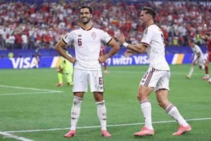 Spain midfielder Mikel Merino #6 smiles with hands on hips as he celebrates his team's first goal during the 2026 World Cup round of 16 match between Portugal and Spain at Dallas Stadium in Arlington on July 6, 2026. A Spain teammate in jersey #8 approaches to congratulate him.
