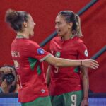 Two female soccer players in red and green uniforms hug and celebrate on the pitch  trybalnews