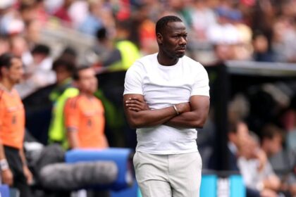 Senegal head coach Pape Thiaw stands on the touchline with his arms crossed, looking intently toward the pitch during the FIFA World Cup 2026 Round of 32 match between Belgium and Senegal at Seattle Stadium in Seattle, Washington, on July 1, 2026.