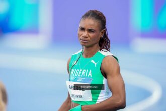 Nigerian female sprinter in green-and-white kit on a track, bib reads GEORGE, looking focused.
