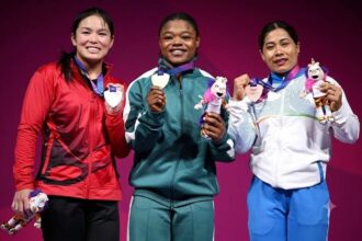Gold medalist Rafiatu Folashade Lawal of Team Nigeria stands center in green, with silver medalist Ann Sophie Taschereau of Team Canada in red on left and bronze medalist Bindyarani Devi Sorokhaibam of Team India in white and blue on right, holding medals and mascots on the podium during the Women's 58kg Weightlifting medal ceremony at the Glasgow 2026 Commonwealth Games at SEC Armadillo on July 27, 2026.