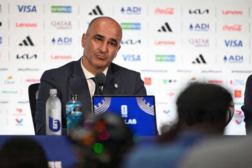 Roberto Martinez head coach of Portugal sits at a press conference table after the FIFA World Cup 2026 Round of 16 match against Spain at Dallas Stadium in Arlington Texas on July 6 2026 He wears a dark suit and tie in front of a sponsor backdrop with a microphone water bottles and a World Cup laptop in front of him  trybalnews