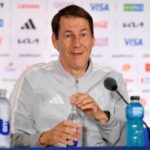 Male coach at a press conference wearing a gray jacket with Argentina crest speaking into a microphone with water bottles on the table  trybalnews