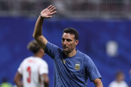Argentina head coach Lionel Scaloni, wearing a light blue Argentina training shirt with the AFA crest, applauds fans with his right hand raised. He stands on the pitch after Argentina's 2-1 win during the FIFA World Cup 2026 Semi Final against England at Atlanta Stadium, Atlanta, Georgia on July 15, 2026.