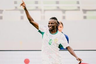 Soccer player in white and green jersey with number 6 celebrating, right arm raised in the air on the field