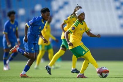 Soccer players in blue and yellow chase the ball on a green field during a match.