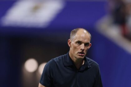 Man in a dark polo on a tennis court, looking focused against a blue background.