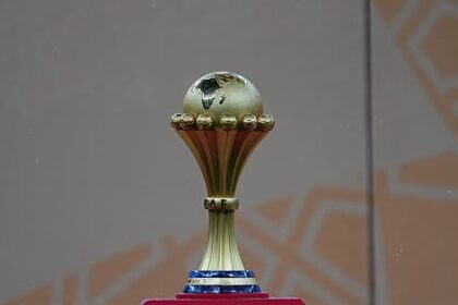 Gold trophy with a small globe on top, displayed on a pink pedestal.