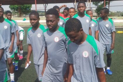 A group of young male soccer players in gray and green jerseys standing in a line on a turf field.