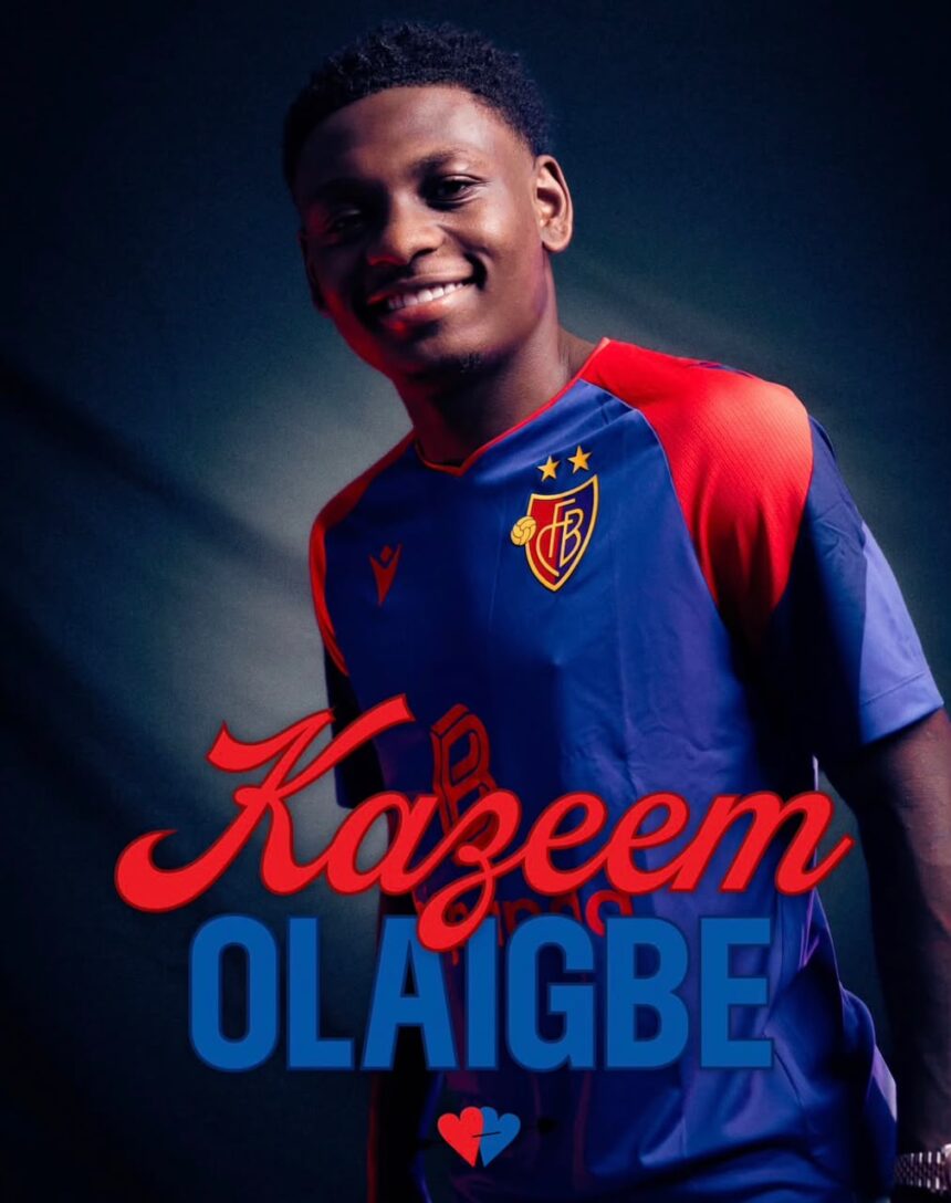 Portrait of a smiling man in a blue red football jersey with a crest featuring the name Kazem Olaigbe in red script and blue block letters in the foreground  trybalnews