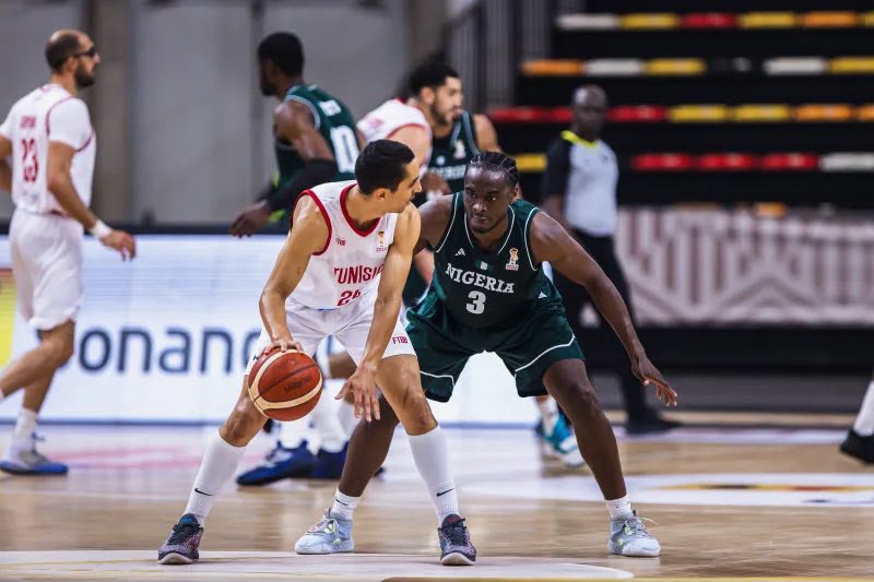 Two basketball playersone in a white Tunisia jersey and one in a green Nigeria jerseycontest the ball on the court  trybalnews