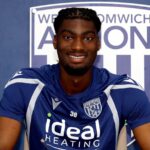 Smiling footballer in a blue West Bromwich Albion jersey signs a document at a table  trybalnews