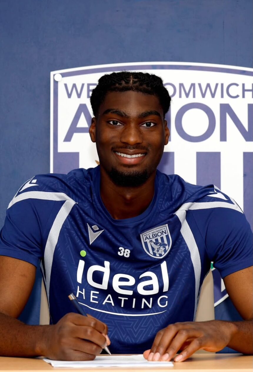 Smiling footballer in a blue West Bromwich Albion jersey signs a document at a table  trybalnews