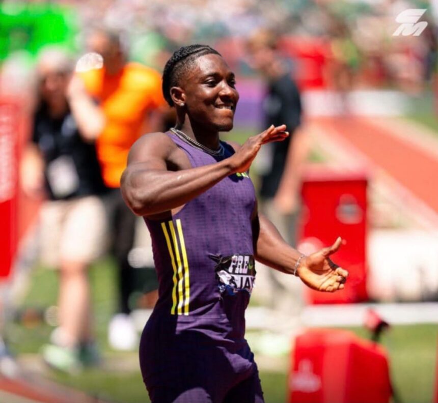 Male sprinter in a purple singlet finishes a track race smiling with arms raised in celebration as fans blur in the background  trybalnews