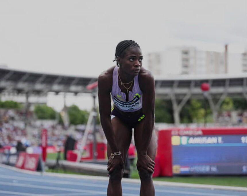 Female sprinter bending over at the track catching her breath during a race with stadium stands and scoreboard in the background  trybalnews