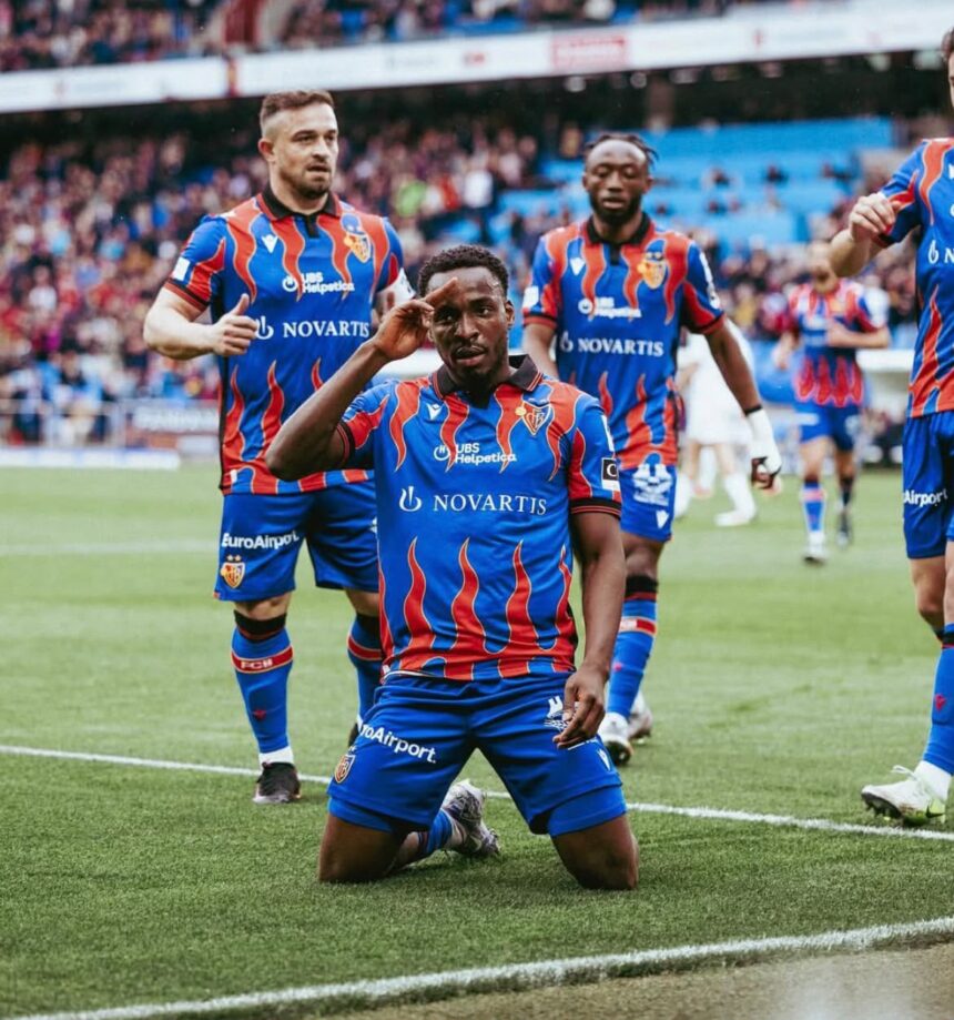 Soccer players in blue and red striped uniforms celebrate on a grassy pitch the central player kneels and salutes while teammates stand behind with a cheering crowd in the background  trybalnews