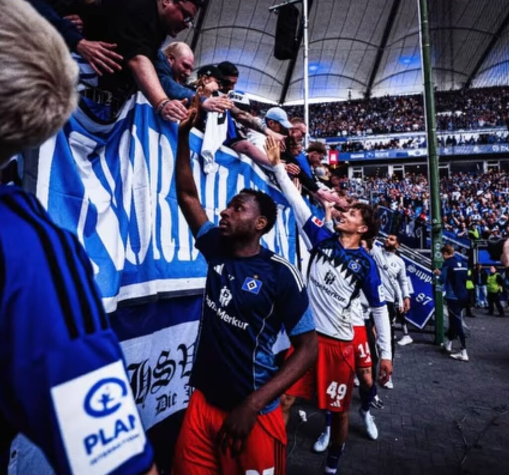 Philip Otele Trybal News Soccer players in blue and white uniforms high five fans over a barrier as a full stadium cheers them on the sidelines trybalnews
