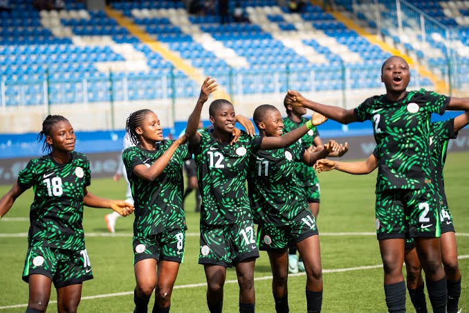 A soccer team in green uniforms celebrates together on the field raising arms in a victory cheer with blue stadium seats in the background  trybalnews