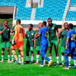 Soccer players in green uniforms line up to shake hands with blue team players before kickoff on a sunny stadium field  trybalnews