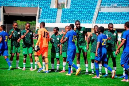 Soccer players in green uniforms line up to shake hands with blue-team players before kickoff on a sunny stadium field.