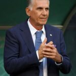 Older man in a navy suit and light blue patterned tie hands clasped looking to the side against a green background  trybalnews