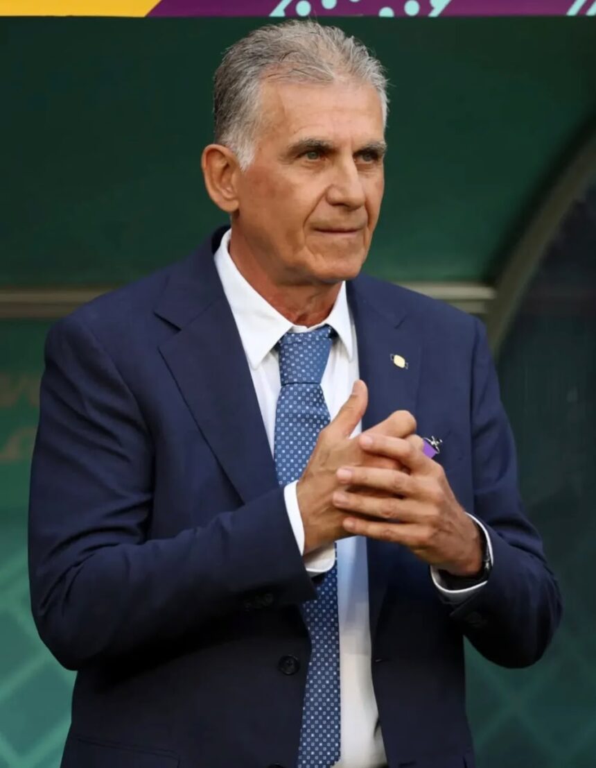 Older man in a navy suit and light blue patterned tie hands clasped looking to the side against a green background  trybalnews