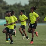 Group of female soccer players in neon training kits sprinting on a football field with a coach supervising  trybalnews