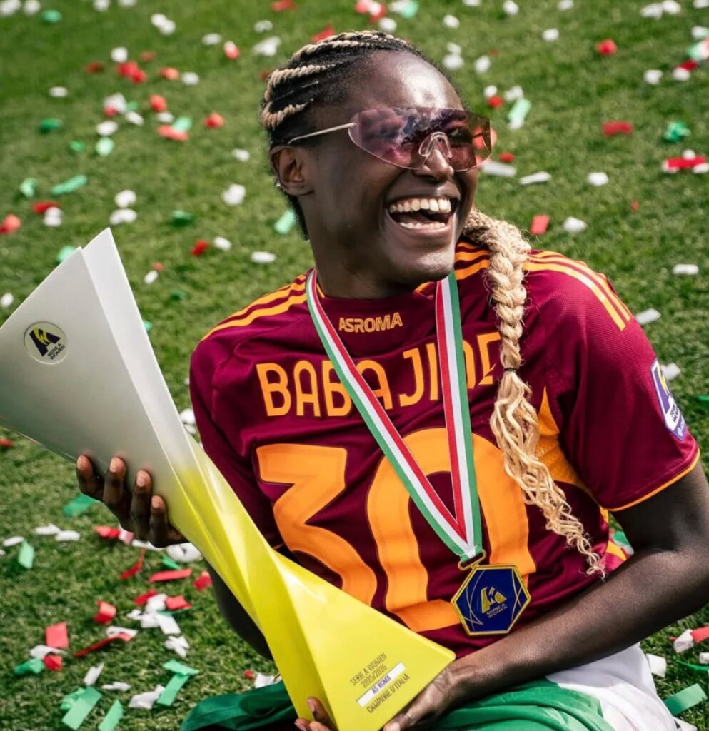 Babajide Rinsola Trybal News Young athlete in maroon and orange uniform smiling with a medal holding a trophy on a confetti strewn field trybalnews