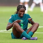 Female soccer player in a green jersey with number 2 sits on the grass pointing to her chest  trybalnews