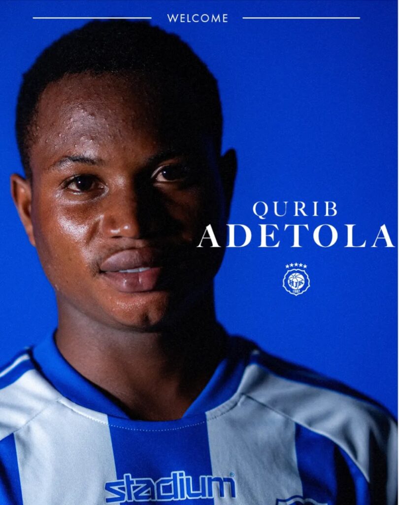 Qurib Adetola Trybal News Close up portrait of a young man in a blue and white striped football jersey against a vivid blue background with QURIB ADETOLA and a team crest overlayed trybalnews