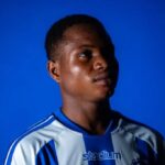 Young man in a blue and white striped sports jersey gazes upward against a solid blue background  trybalnews