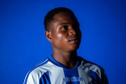 Young man in a blue and white striped sports jersey gazes upward against a solid blue background.
