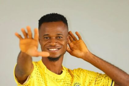 Smiling man in a bright yellow sports jersey cupping his hand to his ear as if listening intentively.