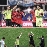 Soccer referee raises a yellow card as a red clad player argues with teammates and a neon clad goalie watches nearby on the field  trybalnews