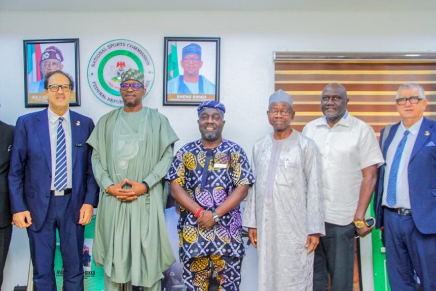Group of six men in formal and traditional attire posing for a photo indoors with Nigerian flags and official portraits in the background  trybalnews