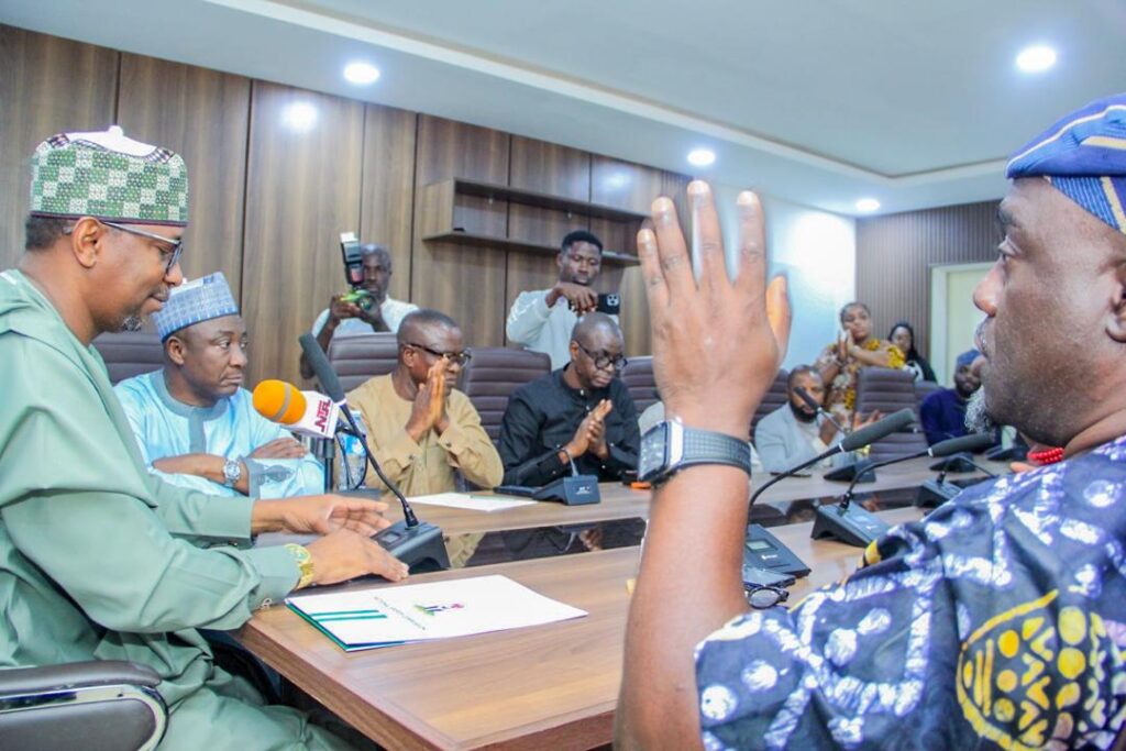 WhatsApp Image 20260709 at 182750 Trybal News Man in green traditional attire speaks into a microphone at a conference table as colleagues and journalists watch trybalnews